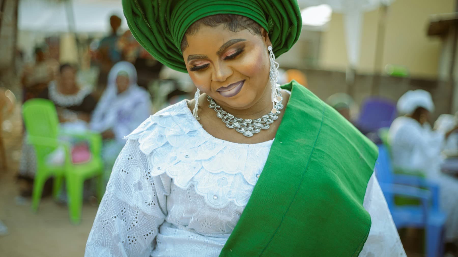 Woman in a white lace outfit and green gele at a celebration in Accra