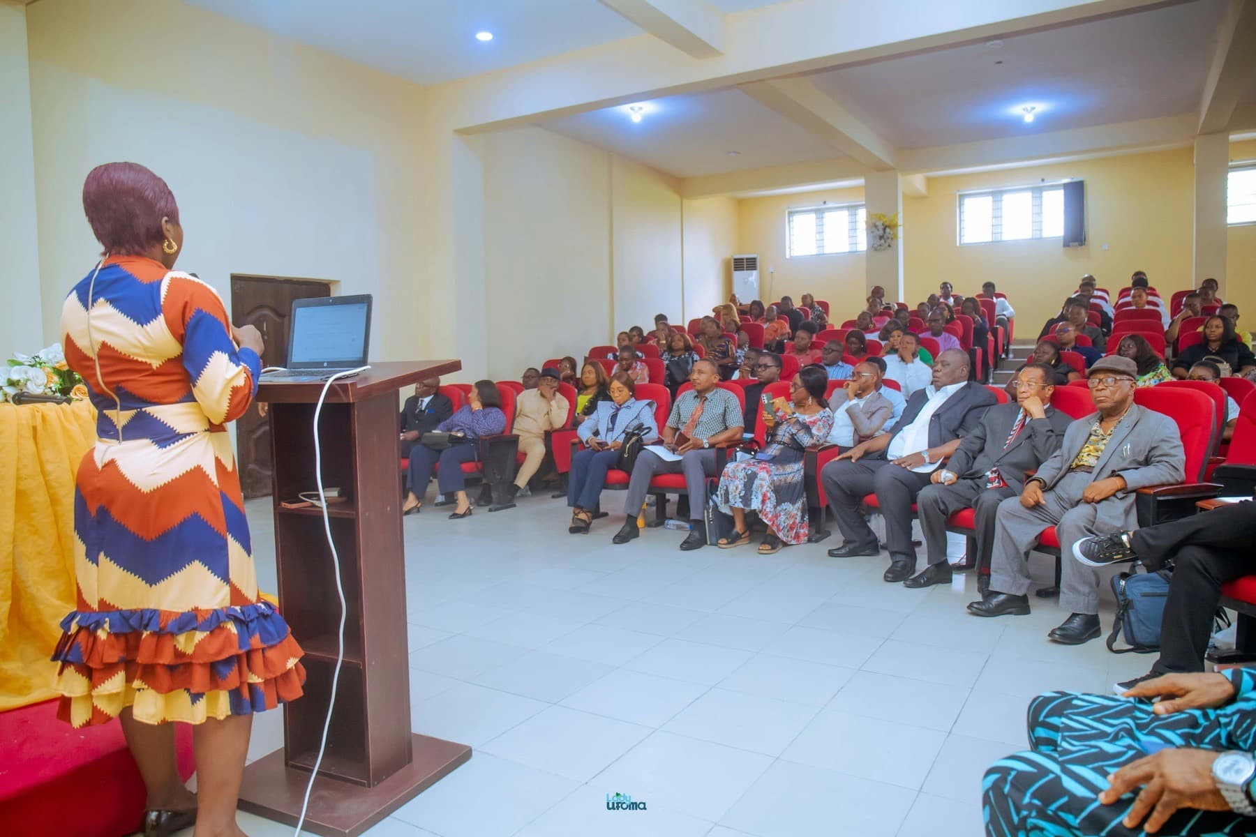 Woman in a patterned dress presenting from a lectern to a full auditorium