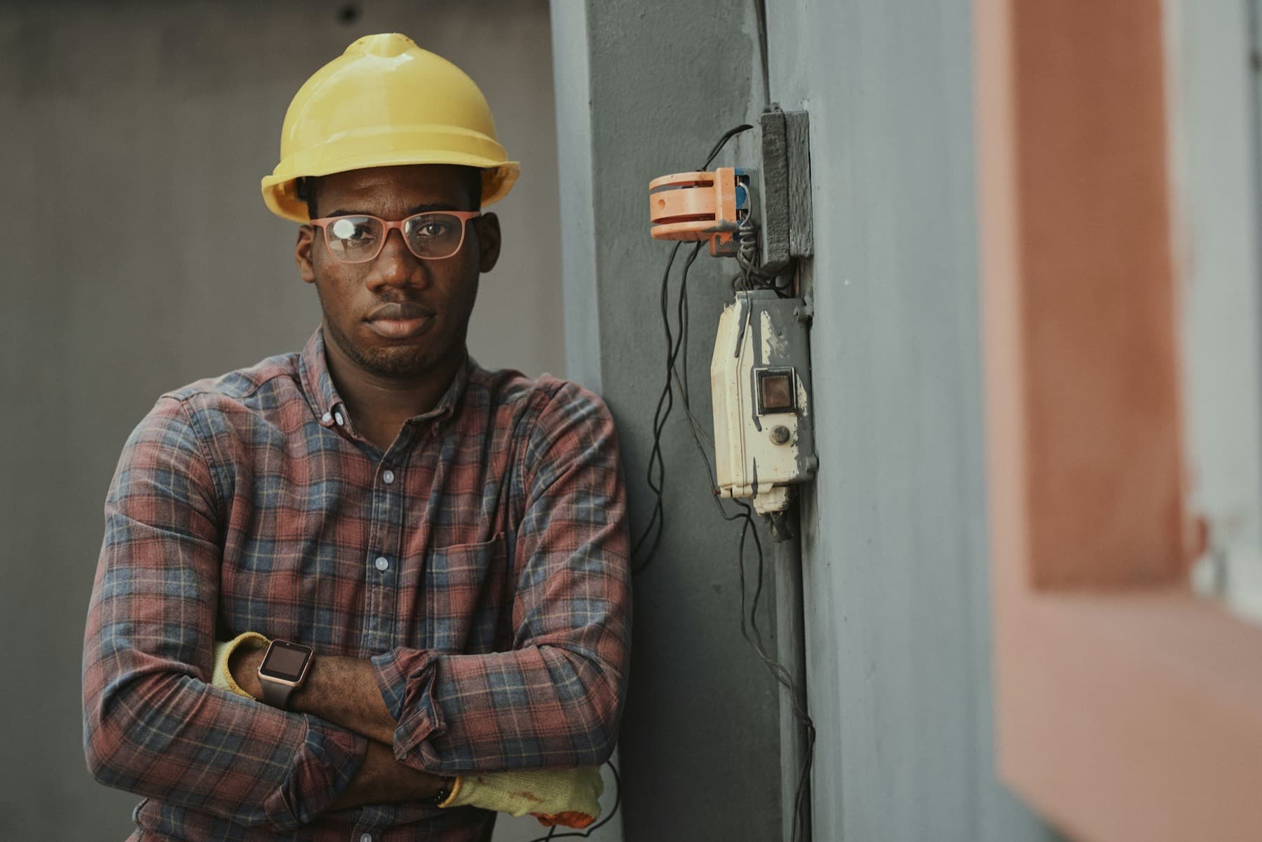 Nigerian engineer in a yellow hard hat and plaid shirt, arms folded, at a site