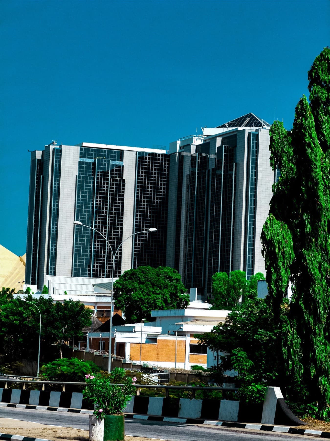 Modern glass office towers and landscaped grounds under a blue sky in Abuja
