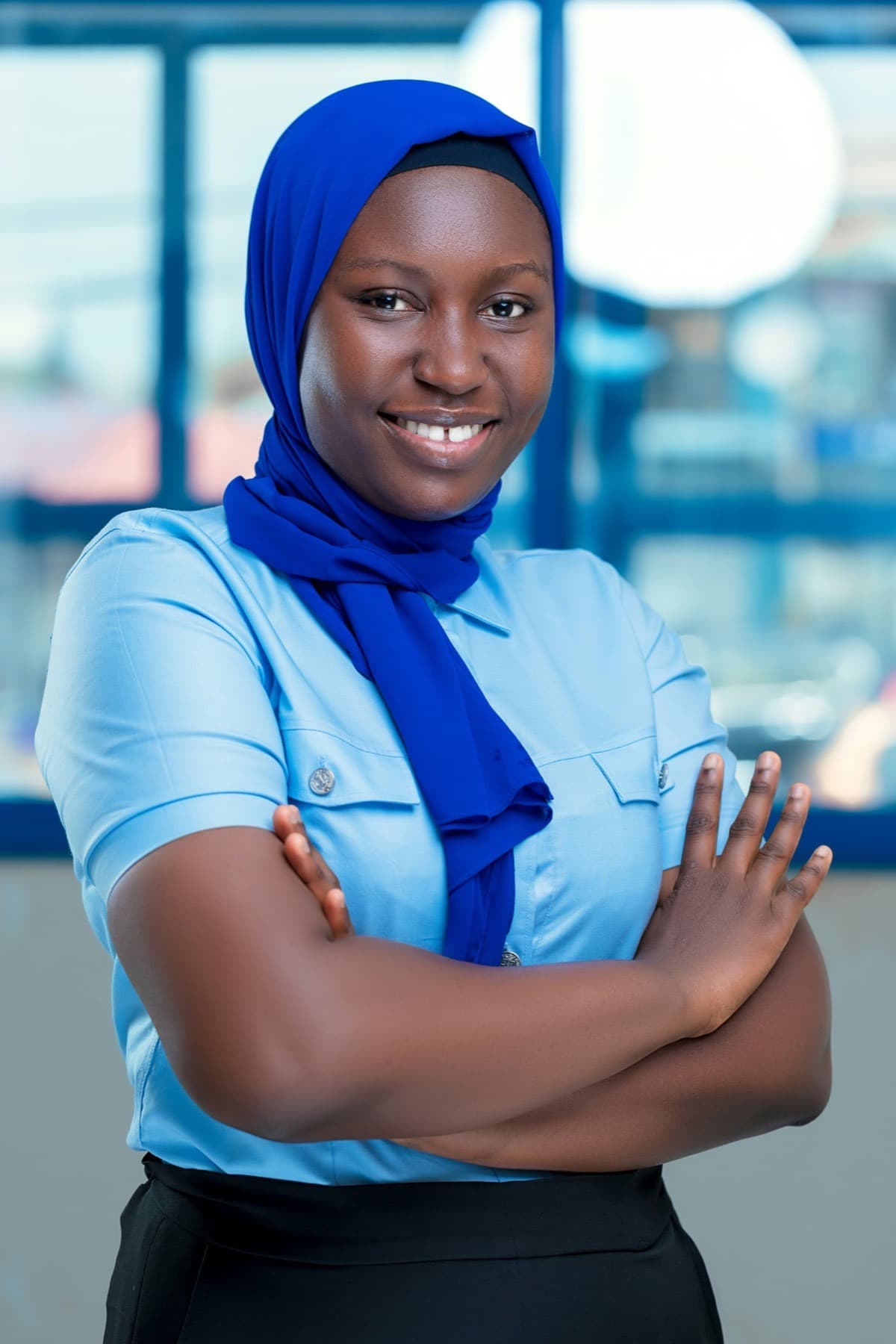 Smiling young professional woman in a navy hijab and light blue shirt, arms folded