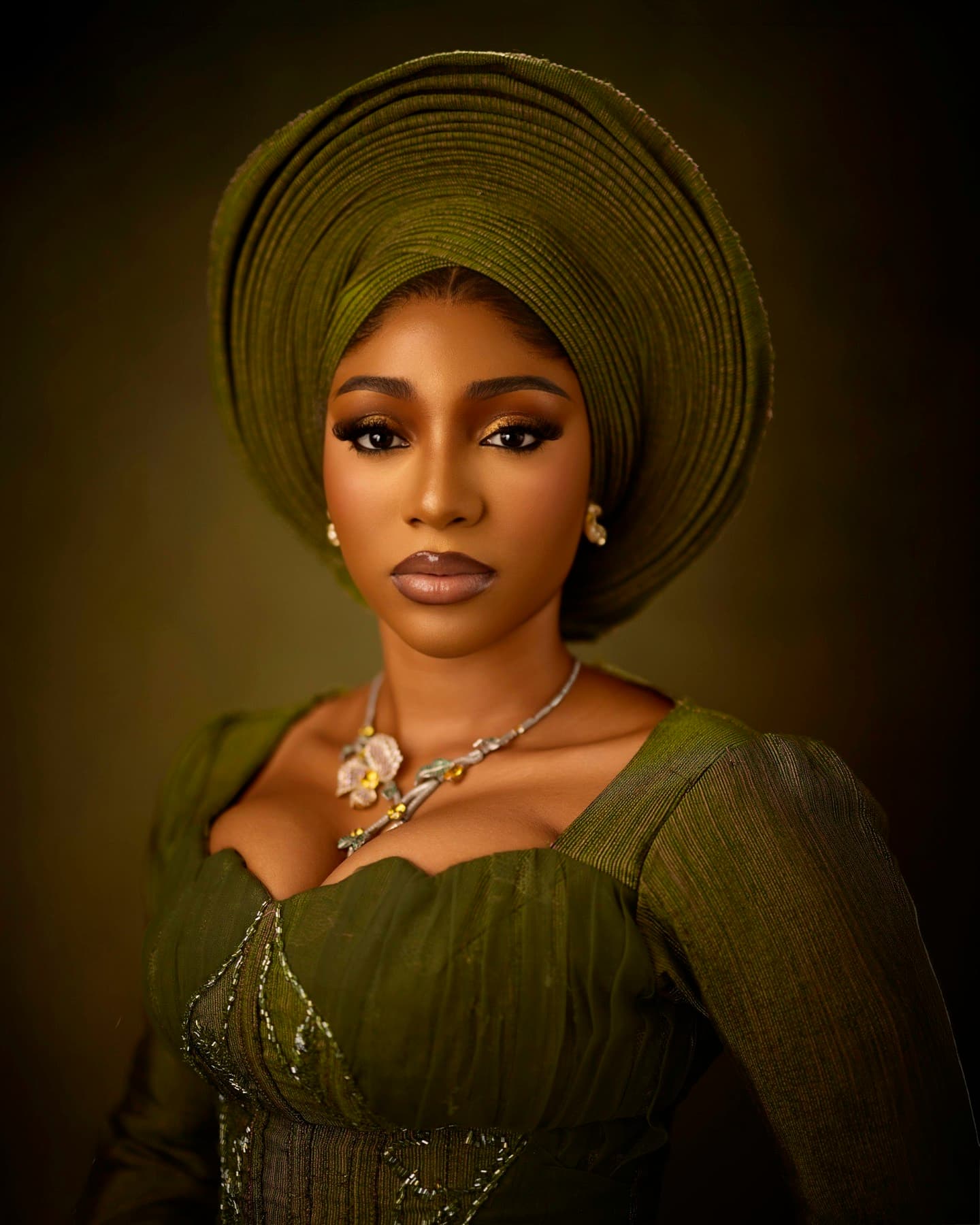 Woman in a green gele and matching dress with a floral necklace